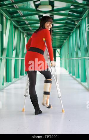 junge Frau mit einem Bein in Gips und Krücken spaziert durch einen Korridor Stockfoto