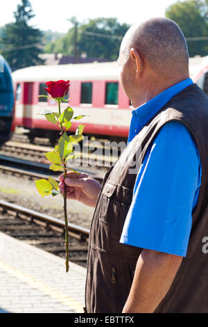 älterer Mann stehen bei der Bahn-Plattform mit einer roten Rose in der hand Stockfoto