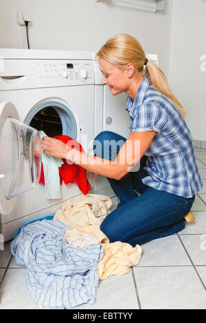 junge Hausfrau vor der Waschmaschine glücklich lächelnd sitzen Stockfoto