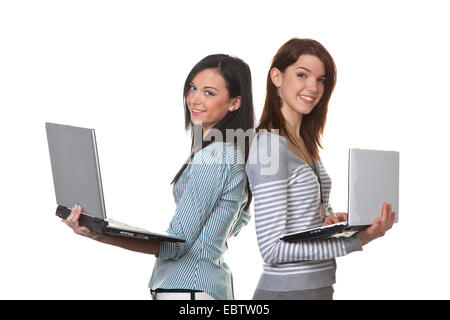 zwei junge Frauen stehen Rücken an Rücken lächelnd mit ihren geöffneten Laptops in Händen Stockfoto