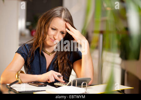 junge Frau nachdenklich sitzen an einem Schreibtisch mit einem Stift in der hand Stockfoto