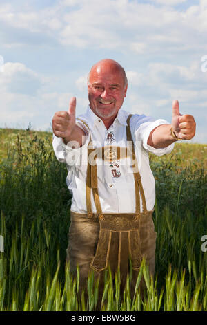 glückliche alte Mann trägt deutsche Tracht mit Daumen nach oben stehend im Getreidefeld, Deutschland, Rheinland-Pfalz Stockfoto