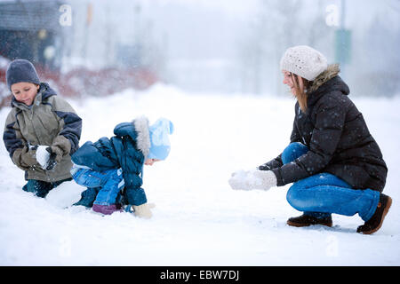 eine Mutter mit ihren zwei kleinen Kindern im Schnee spielen Stockfoto