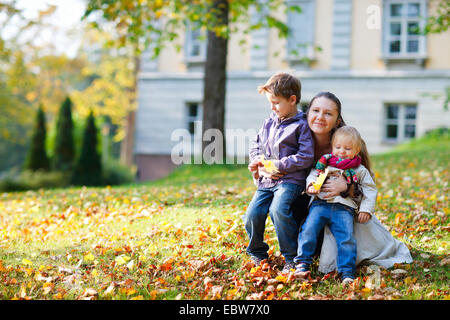 junge Mutter mit ihren beiden Kindern in Wiese im Herbst Stockfoto