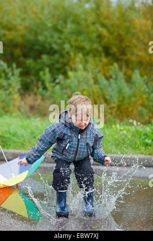 kleiner Junge mit Regenstiefel in einer Pfütze springen Stockfoto