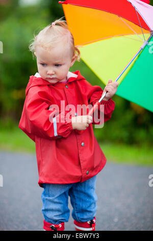 kleines Mädchen in Regenkleidung mit geöffneten Regenschirm Stockfoto