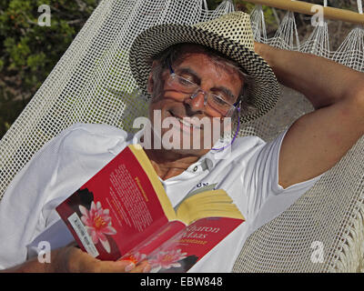 Sonnenbrand, senior in der Hängematte liegen und ein Buch zu lesen Stockfoto