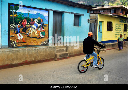 Junge mit dem Fahrrad vorbei an einer auffälligen Wandmalerei bei einer Haus-Fassade, Guatemala, Atitlan See, Santa Cruz la Laguna Stockfoto