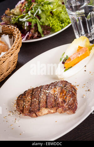 Lecker gegrilltes Rindersteak mit einem gezwirbelten Stück Butter und ein Zweig frischer Rosmarin garniert und serviert auf einem weißen Teller, enge u Stockfoto