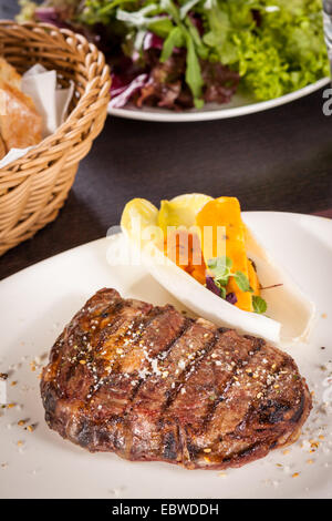 Lecker gegrilltes Rindersteak mit einem gezwirbelten Stück Butter und ein Zweig frischer Rosmarin garniert und serviert auf einem weißen Teller, enge u Stockfoto