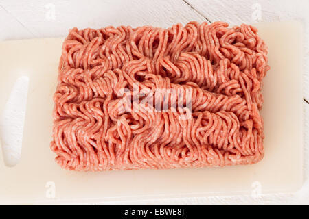 Block von unverpackten kommerzielle Rindfleisch Hackfleisch aus einem Geschäft, die Textur und das Muster des ständigen Ausschusses für Fleischwolf auf weißem Kunststoff Schneidebrett in der Küche verwendet werden Stockfoto