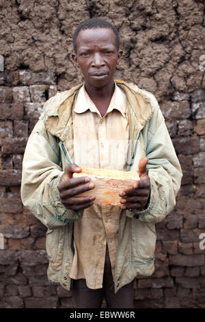 Mann hält ein Protokoll des Holzes und stand vor Schlamm-Mauer, Burundi, Karuzi, Buhiga Stockfoto