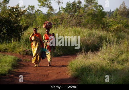 zwei Frauen in traditioneller Kleidung auf den Markt zu Fuß auf einem Pfad durch eine Busch-Landschaft, Burundi, in der Nähe von National Parc De La Ruvubu, Cankuzo Stockfoto