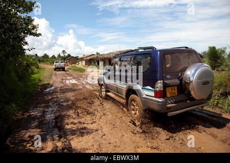 Geländewagen fahren durch eine Schlammgrube unterwegs ein Boden durch Buschlandschaft, die Weitergabe von bescheidenen Hütten, Burundi, Cankuzo, National Parc De La Ruvubu, Cankuzo Stockfoto