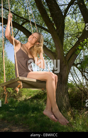 junge Frau in einem Sommerrock sitzen auf einer Wippe Stockfoto