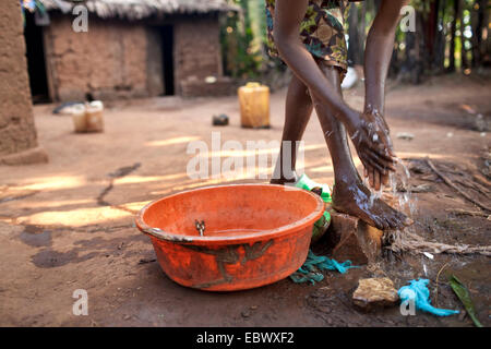 junge Frau in traditioneller afrikanischer Kleidung waschen sich vor ihrem Lehmhaus am Morgen, Burundi, Karuzi, Buhiga Stockfoto