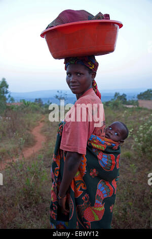 Mutter mit Baby auf dem Rücken transportieren Teller auf dem Kopf, Burundi, Karuzi, Buhiga Stockfoto