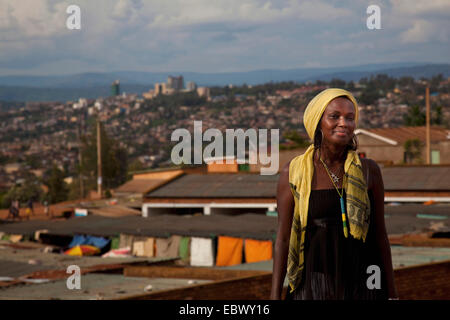 hübsche junge Frau stand lächelnd in vorderen Stadtpanorama mit ärmeren und reicheren Viertel kontrastierende, Ruanda, Nyamirambo, Kigali Stockfoto