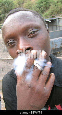 Drogenabhängiger Jugendlicher mit geröteten Augen Rauchen einer Zigarette in der Nähe des Hafens von Goma, Republik Kongo, Nord-Kivu Goma Stockfoto