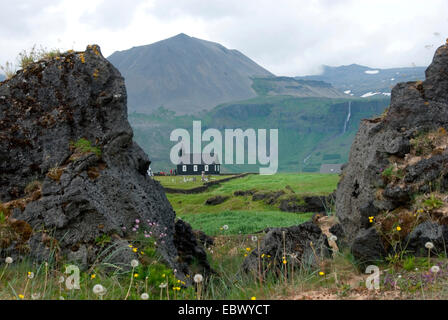 Blick durch zwei Felsen der Lavafeld "Budahraun" auf das hölzerne Kirchlein "Budirkirkja" vor drohenden Bergen, Island, Snaefellsness, B ir Stockfoto