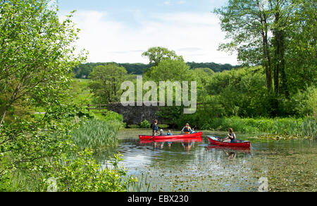 Menschen in zwei hellen roten Kanus paddeln am See, umgeben von grünen Vegetation & Bäume, National Botanic Gardens, Wales Stockfoto