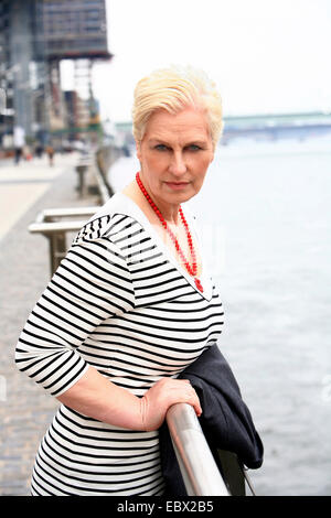 attraktive weißhaarige Frau an einem Rheinpromenade lässig tragen ihre Jacke über einen Arm, Deutschland, Nordrhein-Westfalen, Agrippinawerft, Köln Stockfoto