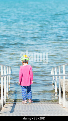 Kleine Mädchen tragen Helm stehend auf Rampe durch Wasser zögern und nachdenken. Stockfoto