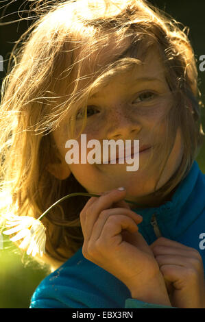 Porträt einer lächelnden 8-jähriges Mädchen mit den Haaren mit ihren Haaren und ein Gänseblümchen in ihrer Hand winkend im Wind, Frankreich Stockfoto