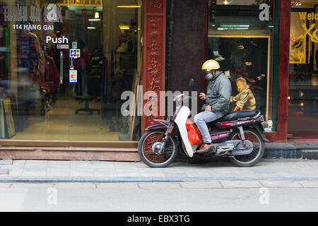 Vietnamesische Mann auf einem Moped-SMS auf seinem Handy. Vor einem Geschäft in Hanoi. Stockfoto