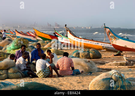 Fischer sitzen am Sandstrand unter ihre Boote und Netze, Chennai, Tamil Nadu, Indien und Marina Beach Stockfoto