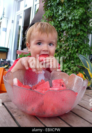 kleiner Junge in einem Kindersitz sitzen Essen Wasser Melone aus einer Glasschale Stockfoto