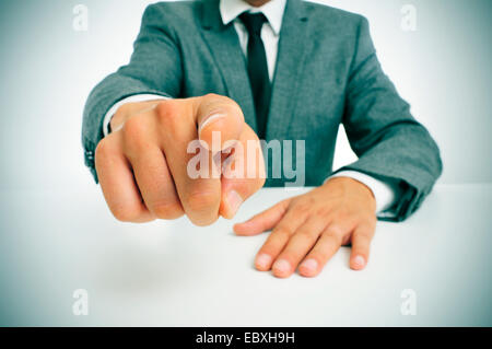 Mann in einem Anzug sitzt in einer Tabelle zeigen mit dem Finger auf den Betrachter Stockfoto