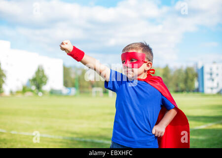 Junge gekleidet in Cape und Maske stehend mit erhobenem Arm und aufrufen Stockfoto