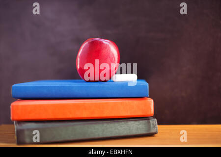 Roter Apfel und Kreide auf Bücher in der Nähe von Blackboard liegend Stockfoto