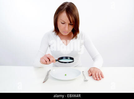 Frau mit Lupe betrachtet Erbse auf Platte Stockfoto