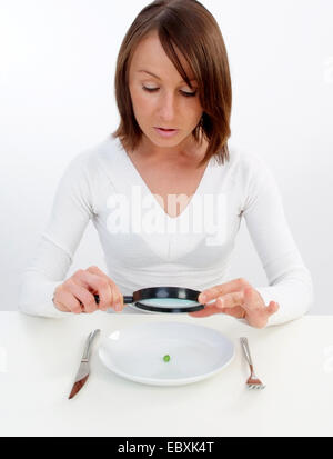 Frau mit Lupe betrachtet Erbse auf Platte Stockfoto