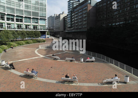 Sonnige Aussicht Leute sitzen sitzen in halb-kreisförmige Fläche von Fluß Irwell am Flussufer Gehweg, Lowry Hotel, Salford, Manchester, UK Stockfoto