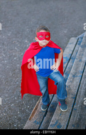 Junge gekleidet in Cape und Maske stehend mit Händen auf den Hüften und nachschlagen Stockfoto