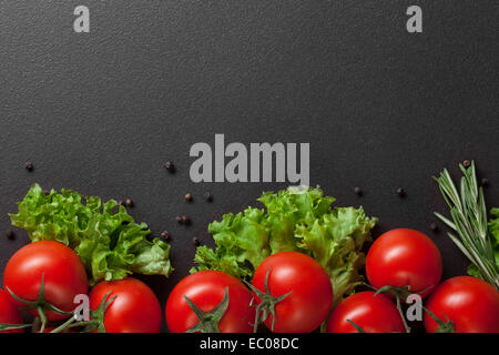 rote Tomaten mit grünem Salat auf schwarz Stockfoto