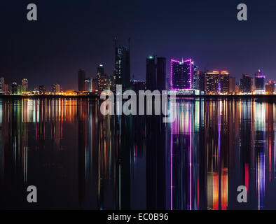Nacht Skyline der modernen Stadt mit leuchtenden Neonröhren und Spiegelbild im Wasser. Manama, der Hauptstadt von Bahrain, Naher Osten Stockfoto