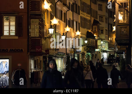 Weihnachts-Einkäufer pass unter festliche Weihnachtsbeleuchtung in der Nacht in Zürichs Altstadt. Stockfoto