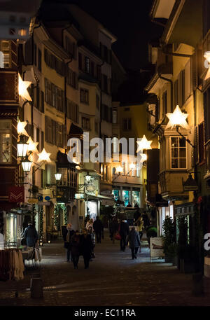 Weihnachts-Einkäufer pass unter festliche Weihnachtsbeleuchtung in der Nacht in Zürichs Altstadt. Stockfoto