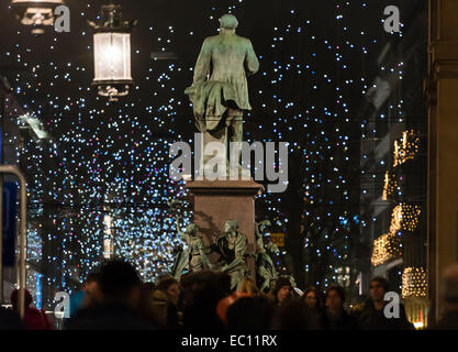 Menschen im Zürcher Hauptbahnhof ziehen vorbei an der Statue von Alfred Escher mit der Stadt Weihnachtsbeleuchtung Glühen in den Rücken. Stockfoto