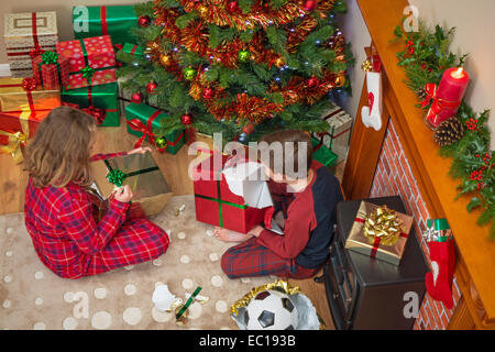 Overhead Foto der Kinder, ein Junge und ein Mädchen, durch den Baum Auspacken der Geschenke an Weihnachten sitzen. Stockfoto