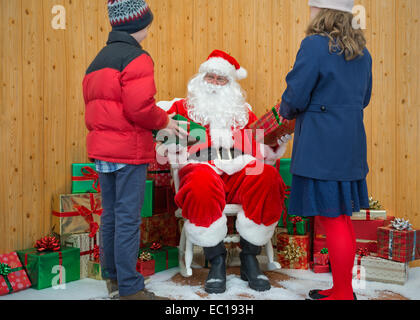 Ein Junge und ein Mädchen erhalten Weihnachtsgeschenke vom Weihnachtsmann in seiner Grotte Stockfoto