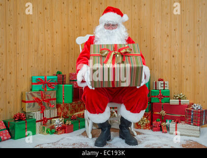 Santa Claus / Weihnachtsmann sitzt in seiner Grotte hält ein Geschenk verpackt für Sie vorhanden. Stockfoto