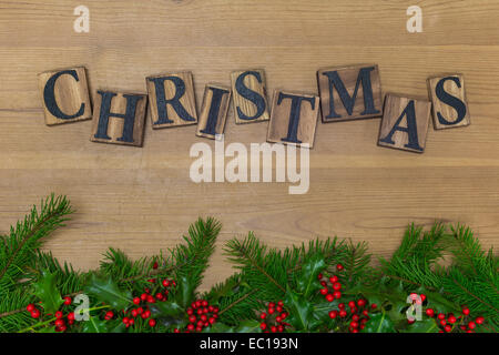 Das Wort Weihnachten in Holz- Buchstaben auf einem rustikalen Hintergrund über ein frisches Grün Girlande mit Stechpalme und Beeren. Stockfoto