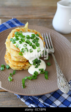 Kartoffelpuffer mit saurer Sahne und Frühlingszwiebeln auf einer Platte, auf Holzbrettern Stockfoto