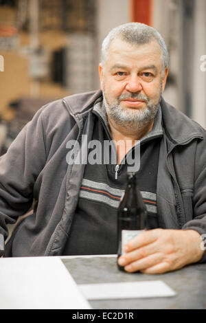 Reifen kaukasischen Mann mit Bier Flasche sitzen an einem Tisch in seinem Geschäft Stockfoto