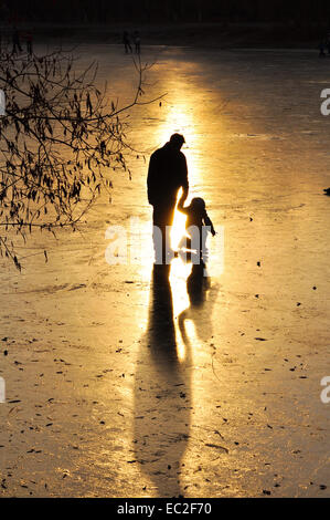 Eisbahn, die Silhouette des Kindes. Eislaufen auf einem zugefrorenen Teich im Licht der untergehenden Sonne. Stockfoto